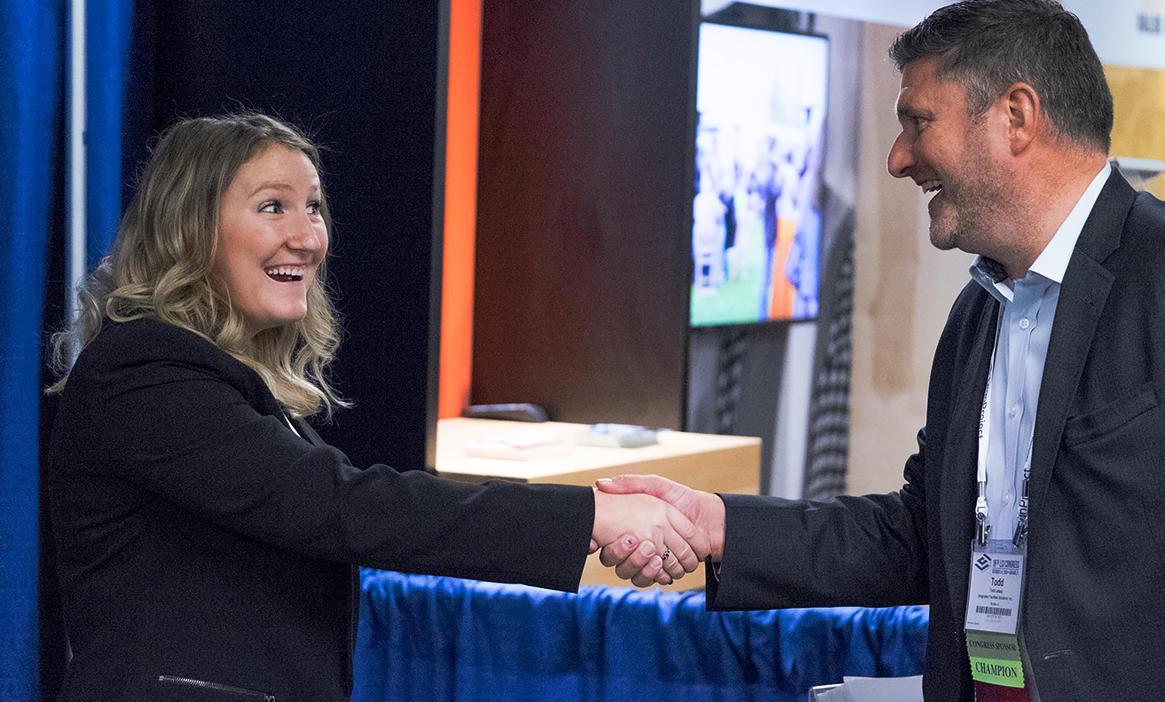 a young woman wearing a black blazer shaking the hand of a man, both smiling