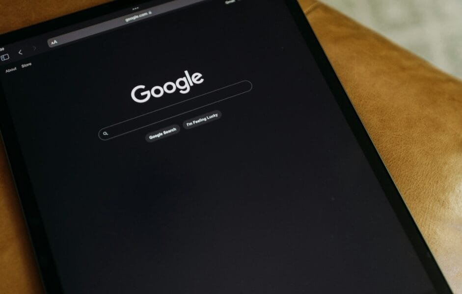 An iPad in dark mode, on the google homepage, tilted at an angle on a wooden table.